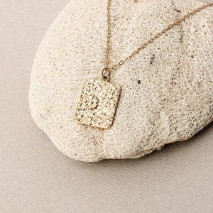 May include: A gold chain necklace with a textured rectangular pendant. The pendant has a hammered or textured finish.