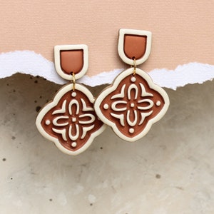 May include: A pair of terracotta and white ceramic earrings with a geometric design. The earrings are dangle style and have a small terracotta top.