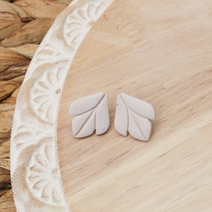 May include: A pair of small, white leaf-shaped earrings. The earrings are made of a textured material and have a subtle, organic look.