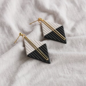 May include: A pair of black and white geometric earrings with gold accents. The earrings are shaped like diamonds and have a textured surface.