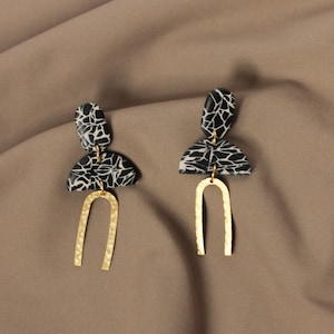 May include: A pair of black and white patterned geometric earrings with gold arch accents.