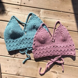 May include: Two crocheted tops, one light blue and one pink, with a v-neck and adjustable straps. The tops are made with a delicate crochet stitch and have a relaxed, bohemian style.