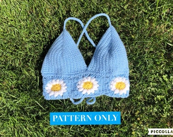 May include: A crochet top in a light blue colour with a daisy pattern. The top has a criss-cross strap design and a tie at the bottom. The text "PATTERN ONLY" is visible at the bottom of the image.