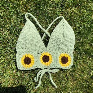 May include: A green crochet crop top with three yellow sunflower appliques.