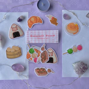 May include: A set of 10 kawaii food stickers featuring various Japanese snacks like takoyaki, onigiri, and taiyaki. The stickers are packaged in a clear plastic bag with a pink and white checkered background and the text "Kawaii Food Stickers Set".