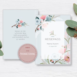 Könnte beinhalten: Eine hellblaue Karte mit einem floralen Design und dem Text "Reisen ist der schönste Weg Geld auszugeben und trotzdem reicher zu werden." Die Karte hat auch einen rosa Kreis mit dem Text "*** mit PERSONALISIERUNG" und eine zweite Karte mit dem Text "mein REISEPASS Marina Norem 14. August 2001".