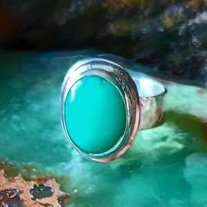 May include: A silver ring with an oval, bright green stone. The ring has a hammered texture on the band and a smooth, polished bezel setting around the stone. The gemstone is a vibrant, solid color.