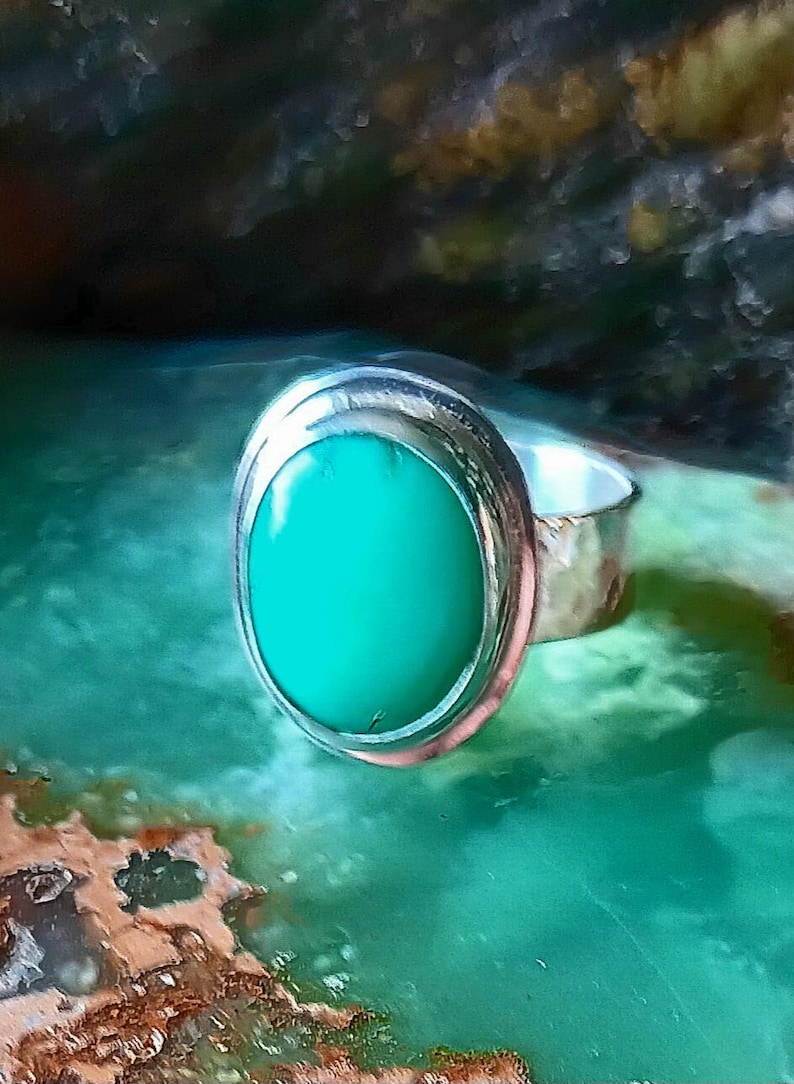 May include: A silver ring with an oval, bright green stone. The ring has a hammered texture on the band and a smooth, polished bezel setting around the stone. The gemstone is a vibrant, solid color.