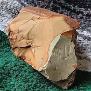 May include: A rough-hewn stone with a layered appearance. The rock features a blend of colors, including tan, brown, and gray, with a textured surface. The stone's edges are jagged, and the overall shape is irregular.