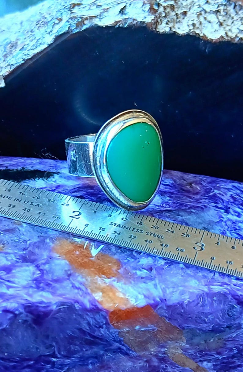 May include: A silver ring featuring a smooth, teardrop-shaped green stone set in a bezel. The ring band has a textured finish with small star cutouts. A stainless steel ruler is positioned alongside, showing the stone width is about 0.75 inches.