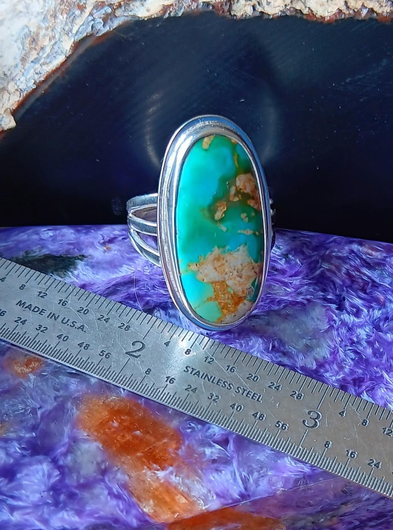 May include: A silver ring featuring a large, oval-shaped turquoise stone with brown matrix inclusions. The ring is positioned next to a stainless steel ruler, showing the stone measures approximately 1.25 inches in length.
