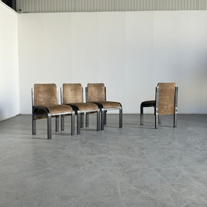 May include: Four black metal chairs with woven brown and tan seats. The chairs are arranged in a row on a gray concrete floor.