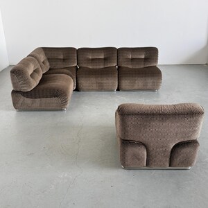 May include: A brown modular sofa and ottoman set. The sofa has a corner configuration with multiple cushioned sections. The ottoman has a matching patterned fabric. The furniture sits on a silver metal base.
