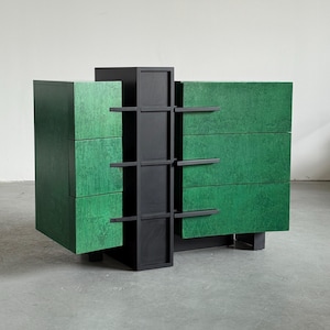 May include: A modern green and black dresser with a unique geometric design. The dresser features three drawers on each side with a textured green finish. A central black structure with shelves and supports adds to the contemporary aesthetic.