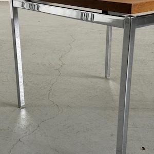 Op de afbeelding: Een vierkante salontafel in mid-century modern stijl. Het tafelblad is warmbruin en de poten en het frame zijn verchroomd. De tafel heeft een minimalistisch ontwerp, met strakke lijnen en een eenvoudig silhouet. De tafel is ongeveer 61 cm lang, 61 cm breed en 46 cm hoog.