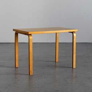 Pode incluir: Uma mesa retangular de madeira clara com uma superfície superior plana e lisa e quatro pernas resistentes. As pernas estão ligadas ao tampo da mesa com suportes de madeira curvos, criando um design limpo e funcional para este móvel.