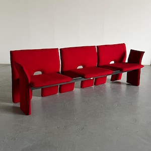 May include: A red modular sofa with four seats and a metal frame. The sofa is upholstered in a red fabric and has a modern design.