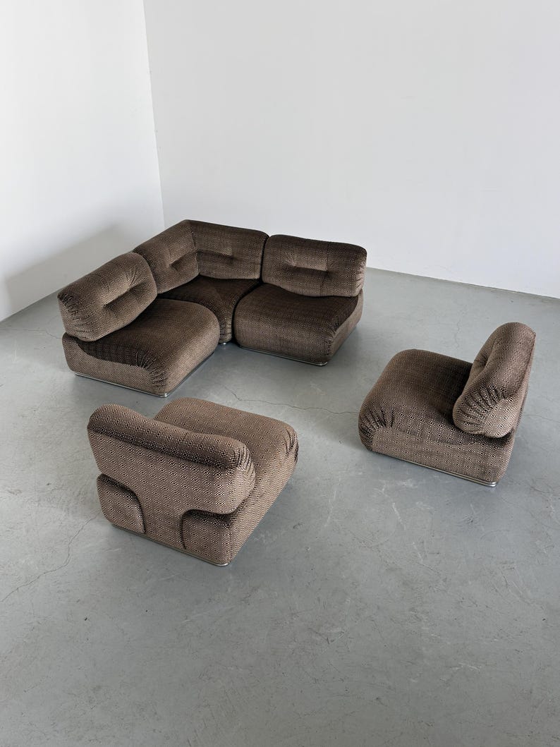 May include: A brown modular sofa set with a corner sectional and two armchairs. The furniture has a textured fabric and a low profile design. The set is placed on a gray floor, creating a modern and stylish living room arrangement.