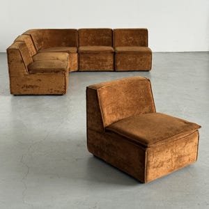 May include: A modular sectional sofa and a matching standalone armless chair upholstered in a textured, burnt orange velvet fabric. The furniture features a low-profile, boxy design with clean lines, square backrests, and thick, cushioned seats.