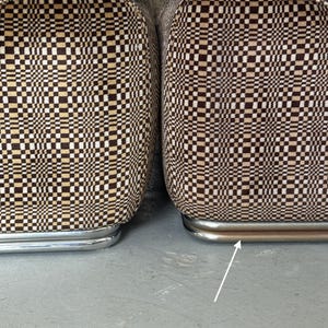 May include: Close-up of two upholstered chairs with a brown, tan, and white checkered pattern. The chairs have a curved, chrome-colored metal base. The fabric pattern creates a retro, geometric design.