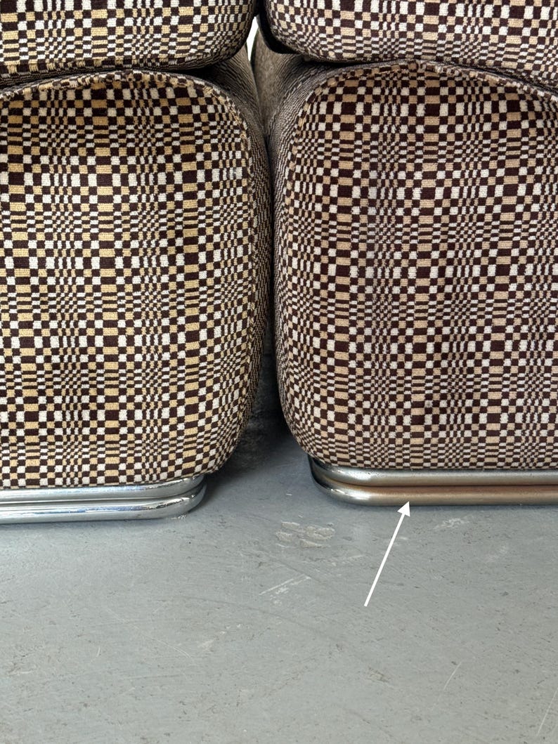 May include: Close-up of two upholstered chairs with a brown, tan, and white checkered pattern. The chairs have a curved, chrome-colored metal base. The fabric pattern creates a retro, geometric design.