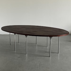 May include: A dark brown oval wooden table with a smooth surface. It has eight silver metal legs. The table is a modern design, suitable for a dining or living room. The table is approximately 240 cm long.