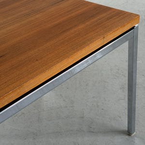 Op de afbeelding: Een salontafel in mid-century modern stijl met een rechthoekig, warm getint houten blad en een geborsteld metalen frame. De tafel heeft een minimalistisch ontwerp, met strakke lijnen en een stevige uitstraling. De poten zijn vierkant.