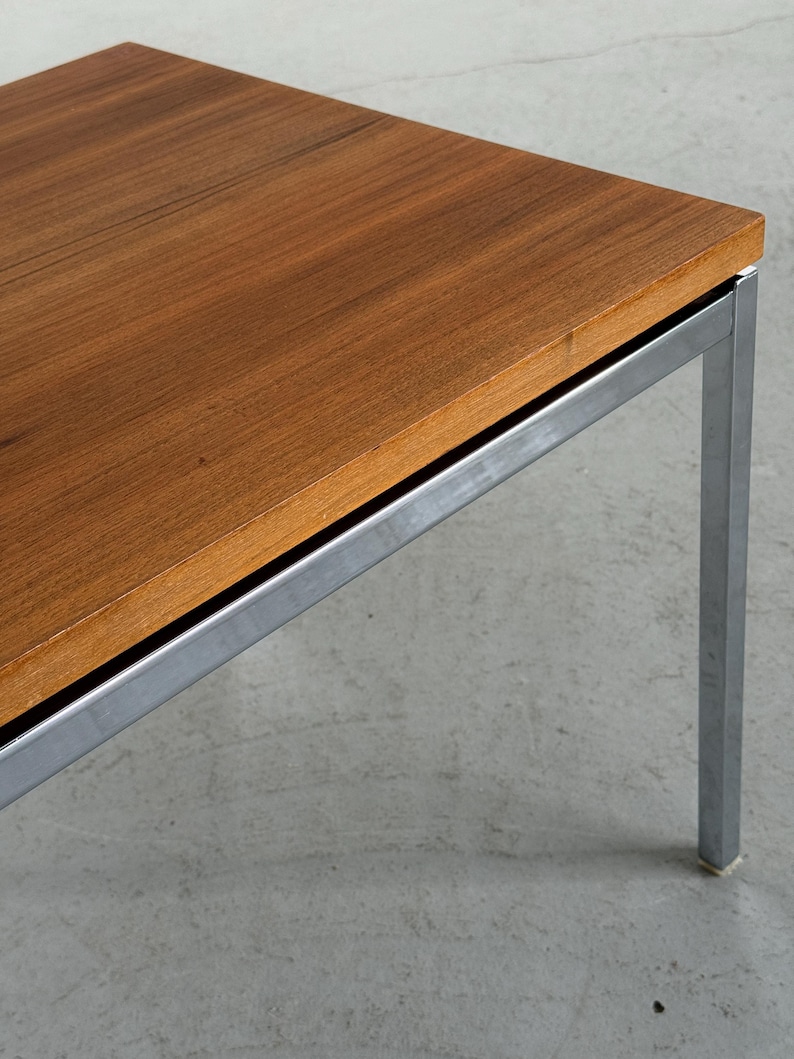 Op de afbeelding: Een salontafel in mid-century modern stijl met een rechthoekig, warm getint houten blad en een geborsteld metalen frame. De tafel heeft een minimalistisch ontwerp, met strakke lijnen en een stevige uitstraling. De poten zijn vierkant.