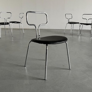 Puede incluir: Conjunto de cinco sillas de comedor de cromo con asientos de cuero negro. Las sillas tienen un diseño simple y moderno con un respaldo curvo y cuatro patas.