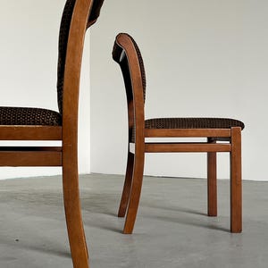 May include: Two wooden chairs with curved backs and brown patterned upholstery. The chairs have a classic design with a warm, natural wood finish. The seats and backs are covered in a textured, dark brown fabric, adding a touch of elegance.