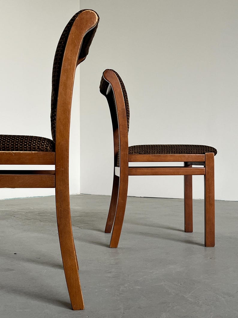 May include: Two wooden chairs with curved backs and brown patterned upholstery. The chairs have a classic design with a warm, natural wood finish. The seats and backs are covered in a textured, dark brown fabric, adding a touch of elegance.
