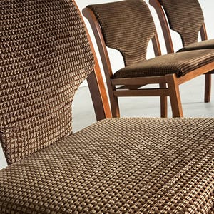 May include: Close-up of three vintage wooden chairs with brown patterned upholstery. The chairs have a classic design with curved backs and seats. The fabric has a textured, woven appearance, and the wood frames are a warm, medium tone.