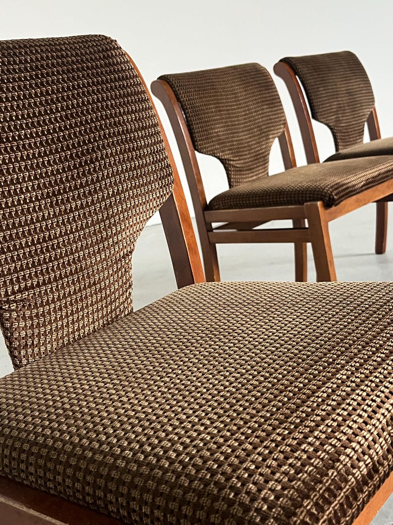 May include: Close-up of three vintage wooden chairs with brown patterned upholstery. The chairs have a classic design with curved backs and seats. The fabric has a textured, woven appearance, and the wood frames are a warm, medium tone.