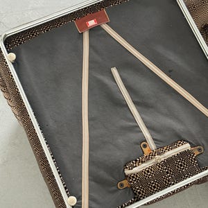 May include: An overhead view of a vintage chair with a brown and black patterned fabric. The chair has a metal frame and a black seat. Beige zippers and a small brown tag are visible.