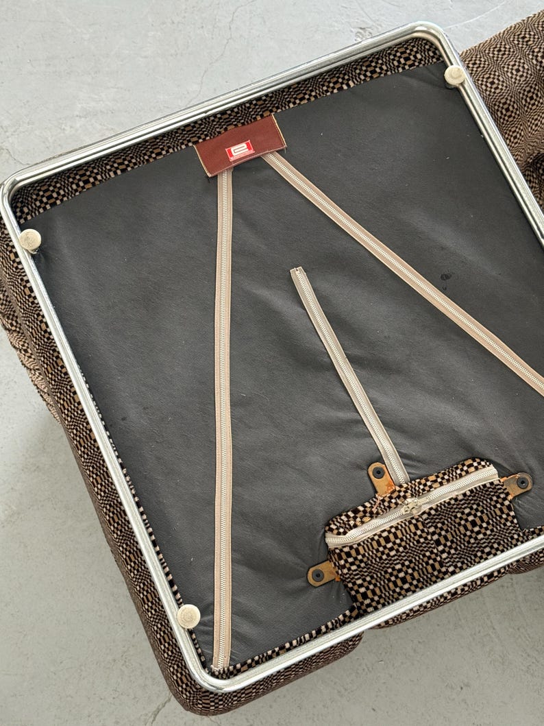 May include: An overhead view of a vintage chair with a brown and black patterned fabric. The chair has a metal frame and a black seat. Beige zippers and a small brown tag are visible.