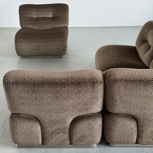 May include: A set of brown upholstered modular seating with a geometric pattern. The set includes a single armchair and a sectional sofa composed of two connected pieces. The furniture has a low profile and rests on a silver metal base.