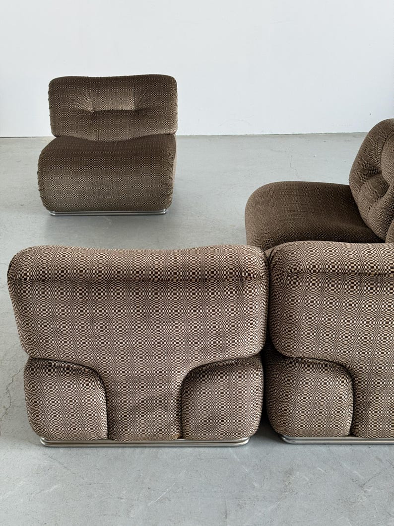 May include: A set of brown upholstered modular seating with a geometric pattern. The set includes a single armchair and a sectional sofa composed of two connected pieces. The furniture has a low profile and rests on a silver metal base.