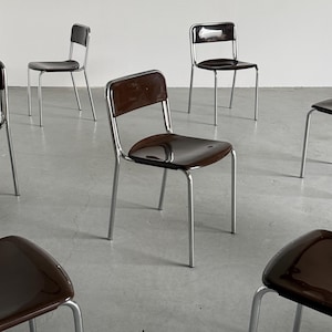 May include: A collection of mid-century modern chairs. Each chair features a dark brown seat and backrest with a chrome-finished metal frame. The chairs are arranged in a room with a neutral-colored floor.