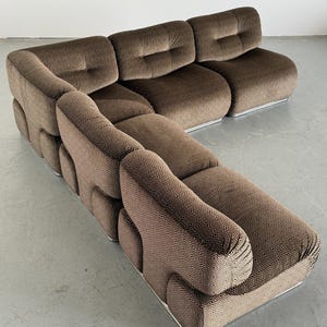 May include: Brown sectional sofa with a patterned fabric and a low profile. The sofa has a rounded design with a silver metal base. The cushions are tufted, and the overall style is modern and comfortable.