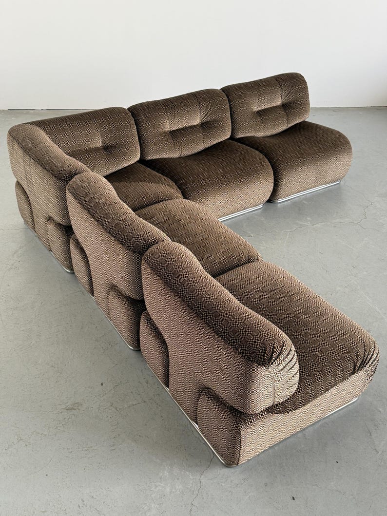 May include: Brown sectional sofa with a patterned fabric and a low profile. The sofa has a rounded design with a silver metal base. The cushions are tufted, and the overall style is modern and comfortable.