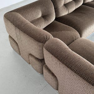 May include: A sectional sofa with a brown and cream geometric pattern. The sofa has a low profile with rounded arms and a tufted back. The base of the sofa is a silver metal.