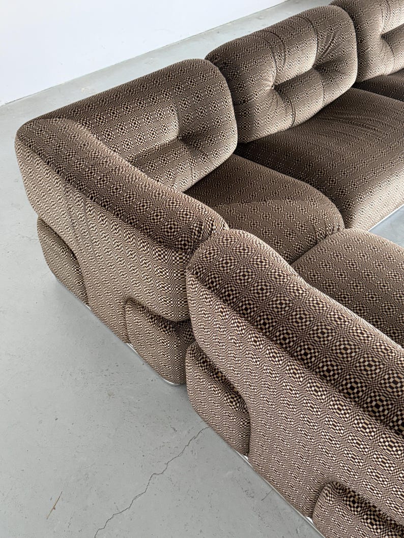 May include: A sectional sofa with a brown and cream geometric pattern. The sofa has a low profile with rounded arms and a tufted back. The base of the sofa is a silver metal.