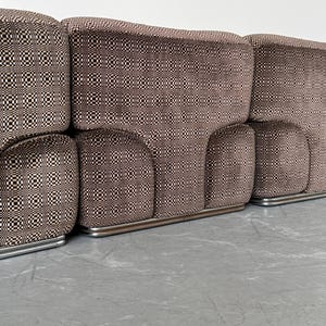 May include: A modular sofa with a brown and black checkered pattern. The sofa has a low profile with rounded armrests and a silver metal base. The fabric has a repeating geometric design.