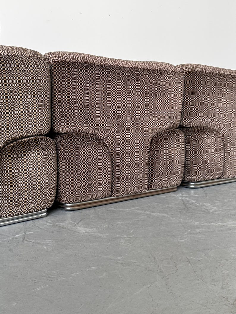 May include: A modular sofa with a brown and black checkered pattern. The sofa has a low profile with rounded armrests and a silver metal base. The fabric has a repeating geometric design.