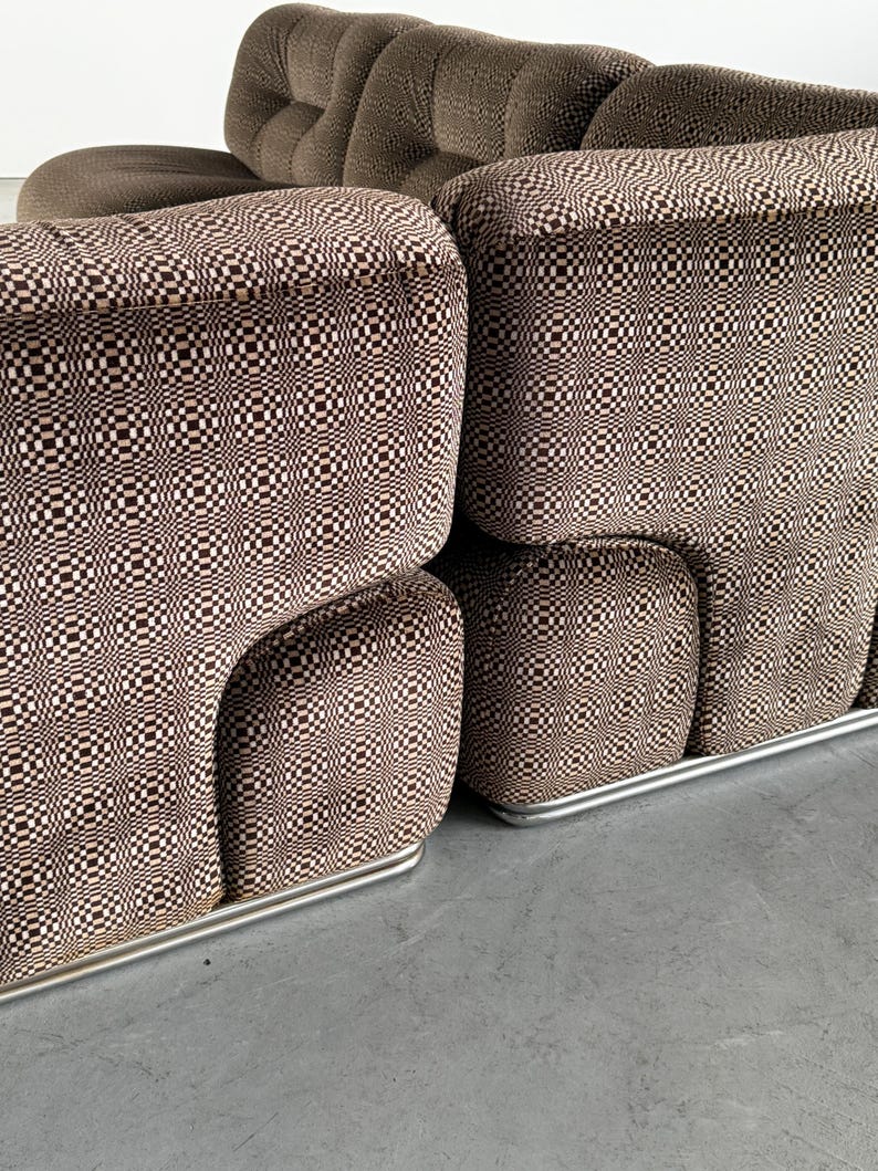May include: A brown and white patterned sofa with a rounded design. The sofa has a checkered pattern on the cushions and a solid brown fabric on the back. The sofa sits on a silver metal base.
