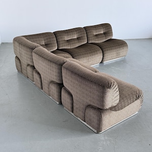 May include: A brown sectional sofa with a patterned fabric. The sofa has a rounded shape with a low profile and a metal base. The cushions are tufted, and the sofa is arranged in an L-shape.