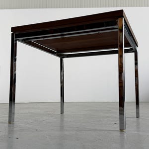 Op de afbeelding: Een bijzettafel in mid-century modern stijl met een donkerbruin houten blad en een verchroomd stalen frame. De tafel is vierkant, ongeveer 46 cm hoog en 61 cm breed.
