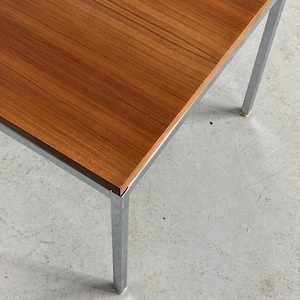 Op de afbeelding: Een rechthoekige houten tafel met een bruin oppervlak en een verchroomd metalen frame. De tafel heeft vier rechte poten. De tafel is ongeveer 76 cm lang en 51 cm breed.