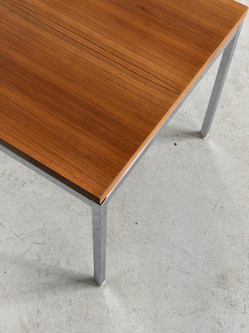 Op de afbeelding: Een rechthoekige houten tafel met een bruin oppervlak en een verchroomd metalen frame. De tafel heeft vier rechte poten. De tafel is ongeveer 76 cm lang en 51 cm breed.