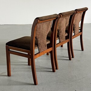 May include: Three wooden chairs with brown woven backs and seats. The chairs have a curved back design and are made of a light-colored wood. The woven material on the backs and seats is a darker brown color, creating a contrast.